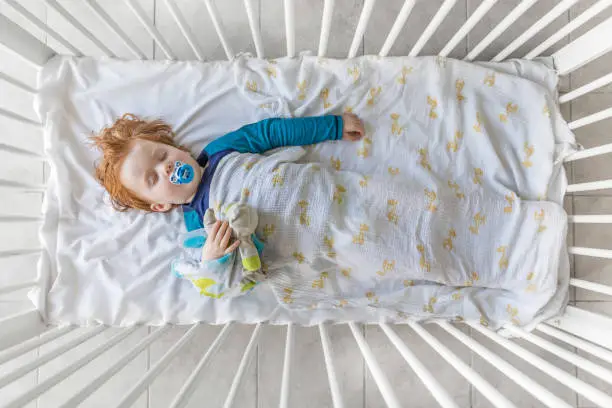 Cute Redhead Baby Boy Sleeping in the Crib with pacifier and security blanket