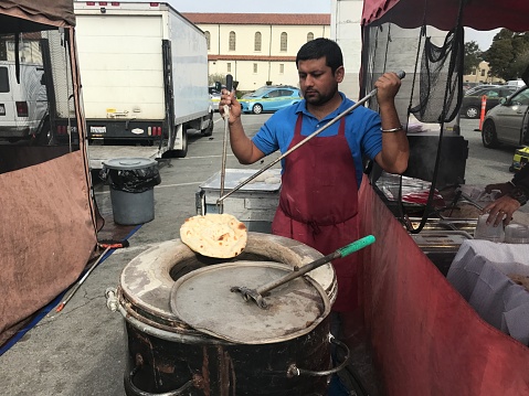 A Indian Gentleman is baking Naan at Farm Market. It is a outdoor farm market on weekend only for small business.
