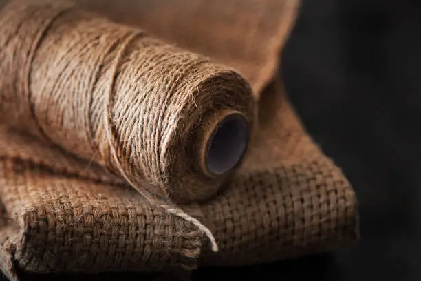 Photo of Natural jute twine roll, burlap on black background. Supplies and tools for handmade hobby leisure