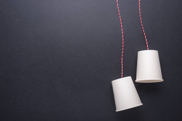 istock Two white paper cup connect with red rope used for classic phone on black stone table board. For old communication system concept 915543780