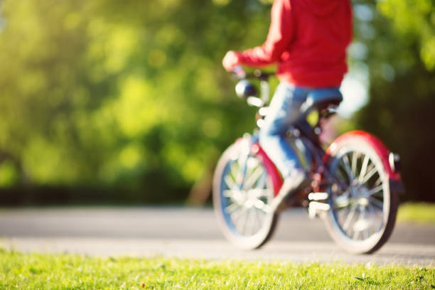 blurred view to a child on a bicycle at asphalt road in summer. Bike in the park. Boy cycling outdoors on beautiful sunny evening