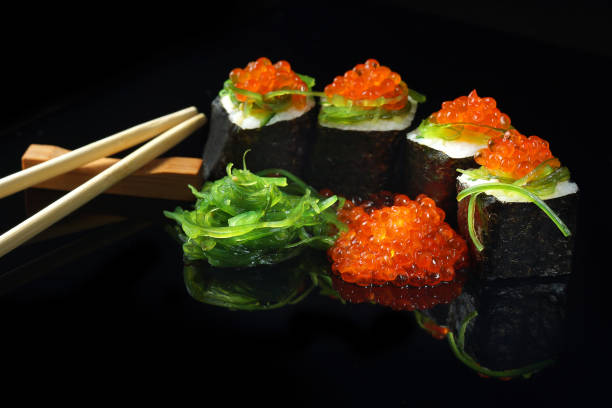 istock Sushi with caviar and algae salad next to chopsticks on a black background with reflection. 915556204