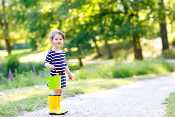 hermoso niño niña jugando en el parque. adorable niño vistiendo ropa casual de moda y botas de goma amarillas. - frog batrachian animal head grass fotografías e imágenes de stock