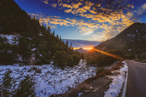 Sunset at snow-covered Mount Baldy in winter with a road winding through the tall peaks and colorful clouds in the sky, San Gabriel Mountains, San Bernardino County, California