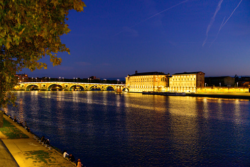 Toulouse, France - October 06, 2017:  The most famous and beautiful stone arch bridge Pont Neuf and 17th century building Hotel Dieu Saint Jacques on the edge of the Garonne river at the dusk in Toulouse, at the South of France. The bridge crossing the Garonne River in the centre of Toulouse and it was built between 1544 and 1632. And the old hospital building was built 17th century.