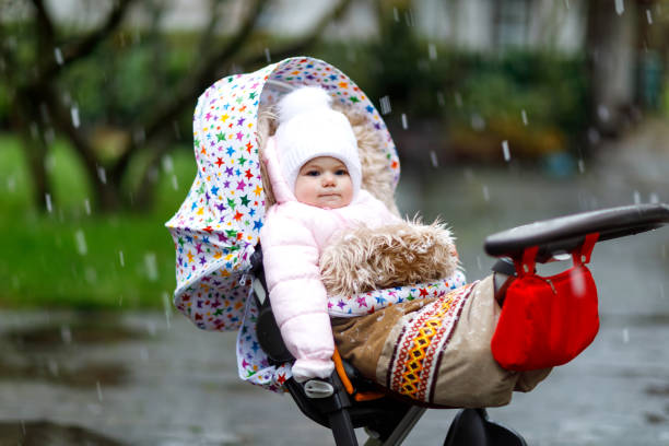 cute little beautiful baby girl sitting in the pram or stroller on cold day with sleet, rain and snow. - smiling little girls little boys autumn imagens e fotografias de stock