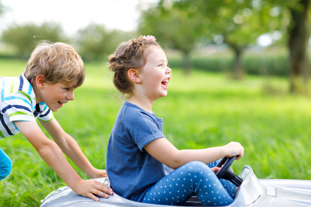 dos niños felices jugando con gran viejo coche de juguete en el jardín de verano, al aire libre - car child teamwork sports race fotografías e imágenes de stock