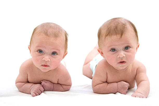 Two babies resting on their stomachs on white sheets stock photo