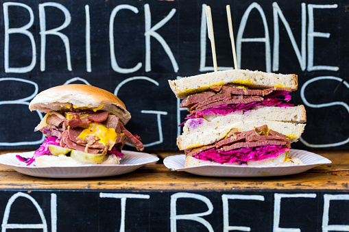 Close up of salt beef and mustard sandwiches with Brick Lane sign in background