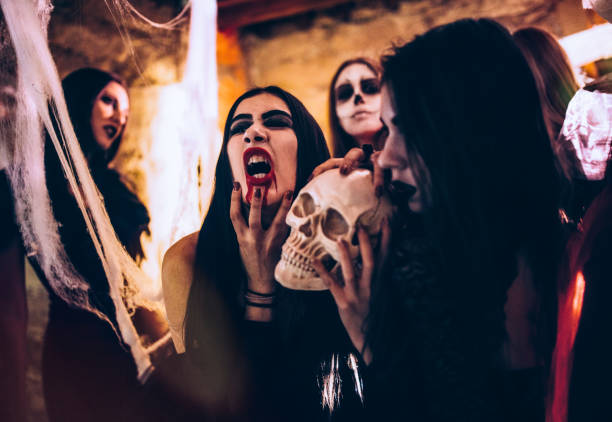 istock Young gothic vampire women holding skull at Halloween party 915620576