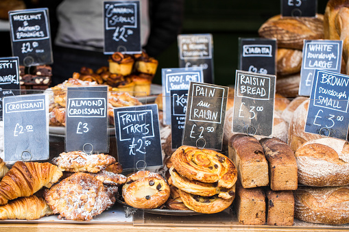 Close up color image depicting a large selection of artisan gourmet breads and pastries displayed on a bakery stall at Borough Market, London, UK, one of the most popular and oldest food markets in the world. Each item is labelled and priced. Room for copy space.