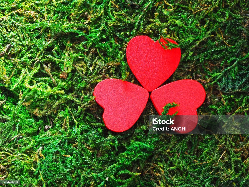 Three red heart shaped objects in form of a clover on the green moss. Red shamrock. Background for St. Patrick's Day celebration Ireland Stock Photo
