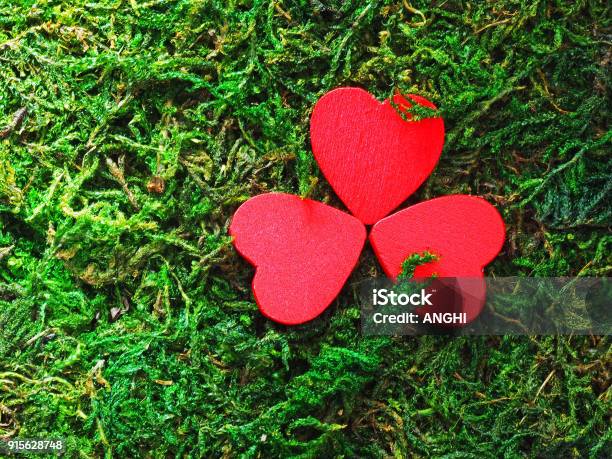 Three Red Heart Shaped Objects In Form Of A Clover On The Green Moss Red Shamrock Background For St Patricks Day Celebration Stock Photo - Download Image Now