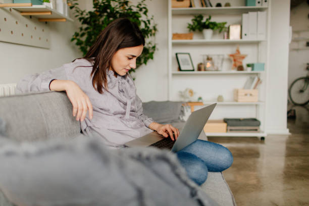 młoda kobieta używająca komputera w domu - wireless technology working at home one person reading zdjęcia i obrazy z banku zdjęć