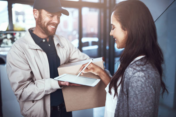 This was simple and easy Shot of a cheerful delivery man handing over a package to a customer and letting them sign on a digital tablet inside a building door to door salesperson photos stock pictures, royalty-free photos & images