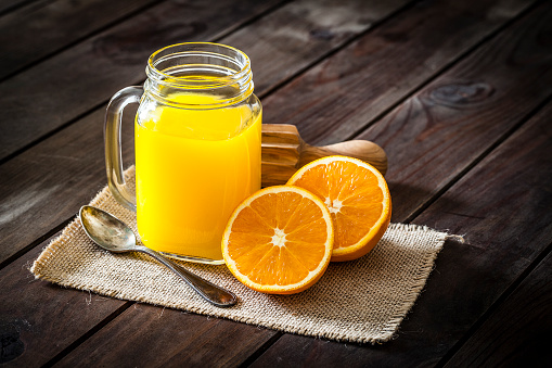 Oranges and orange juice on an old white table with blurred nature in the background, natural light, selective focus.
