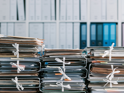 Stacks of files and paperwork in the office and bookshelves on the background: management and storage concept