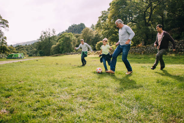 Playing Football With Grandad Three generation family are playing football together in a field. There are two boys, their father and their grandfather. old football stock pictures, royalty-free photos & images