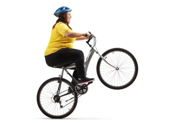 Overweight woman riding a bike and doing a wheelie isolated on white background