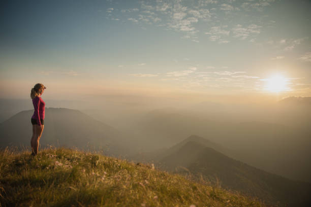 Woamn stands on a peak of mountain at sunset