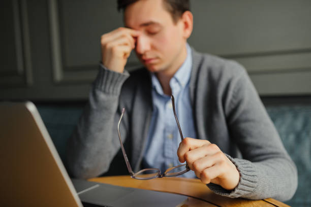 istock Feeling sick and tired. Frustrated young man massaging his nose and keeping eyes closed while sitting while working in cafe. 915677100
