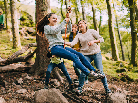 Teenage girl is being pushed on a rope swing in the woods by her family.