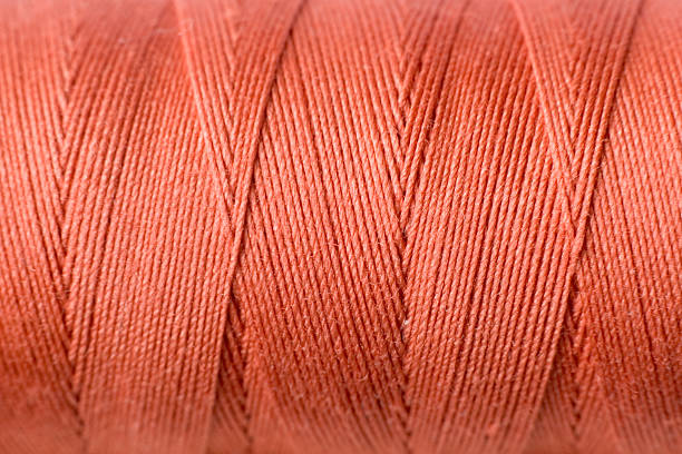 image of a spool of orange thread on a background of rough twine