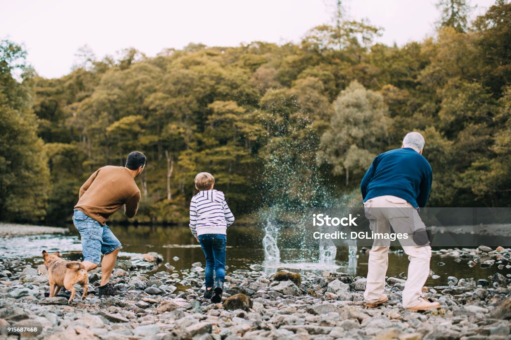 Three Generation Family are Skimming Stones Little boy is skimming pebbles on a lake with his father and grandfather. Family Stock Photo