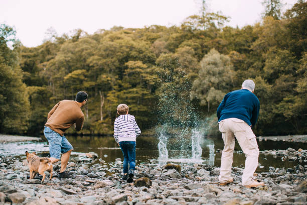 Three Generation Family are Skimming Stones Little boy is skimming pebbles on a lake with his father and grandfather. keswick photos stock pictures, royalty-free photos & images