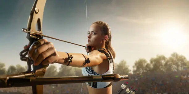 Female archer shooting with the longbow at sunset. Archer in professional field with a lot of fans.