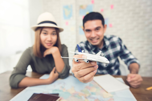 Asian couple planing their vacation trip using the map and playing with a toy model aircraft , getting excited about their  traveling