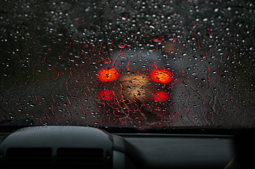 View from a rain-drenched windshield on blurred back lights of a car in front. Heavy rain