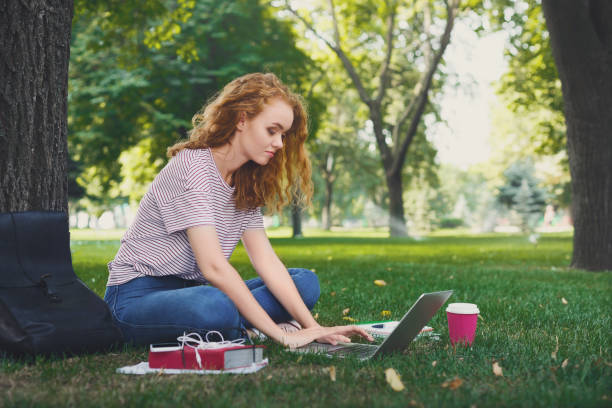 istock Young redhead girl in casual working sitting under a tree 915704380