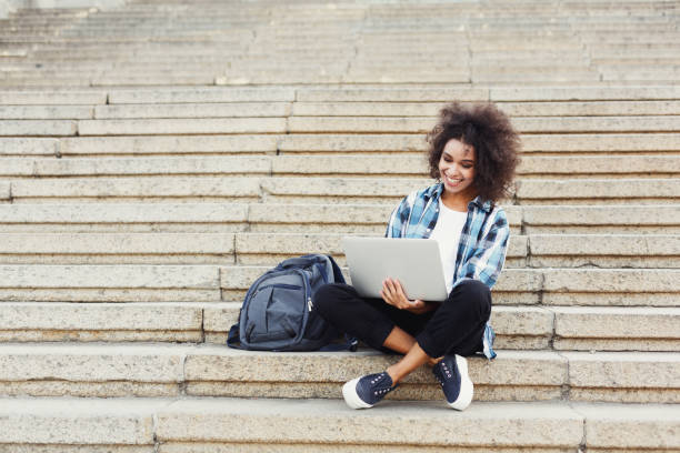 istock Smiling student sitting on stairs using laptop 915708240