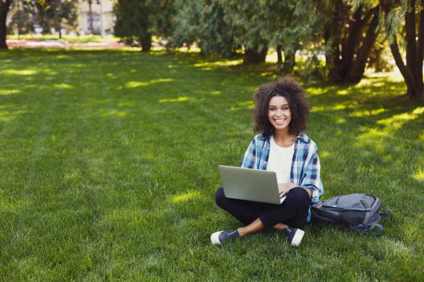 istock Cheerful young woman using laptop in park 915708402