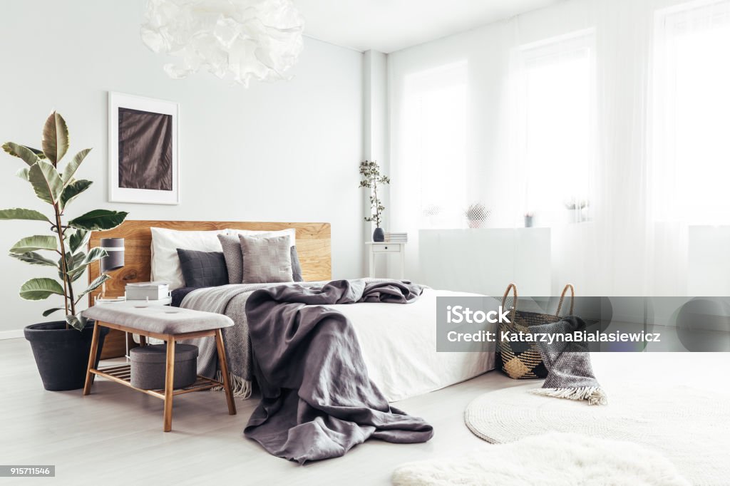 Spacious bedroom with windows White spacious bedroom interior with windows, potted plant and basket with blanket standing by the bed Bedroom Stock Photo