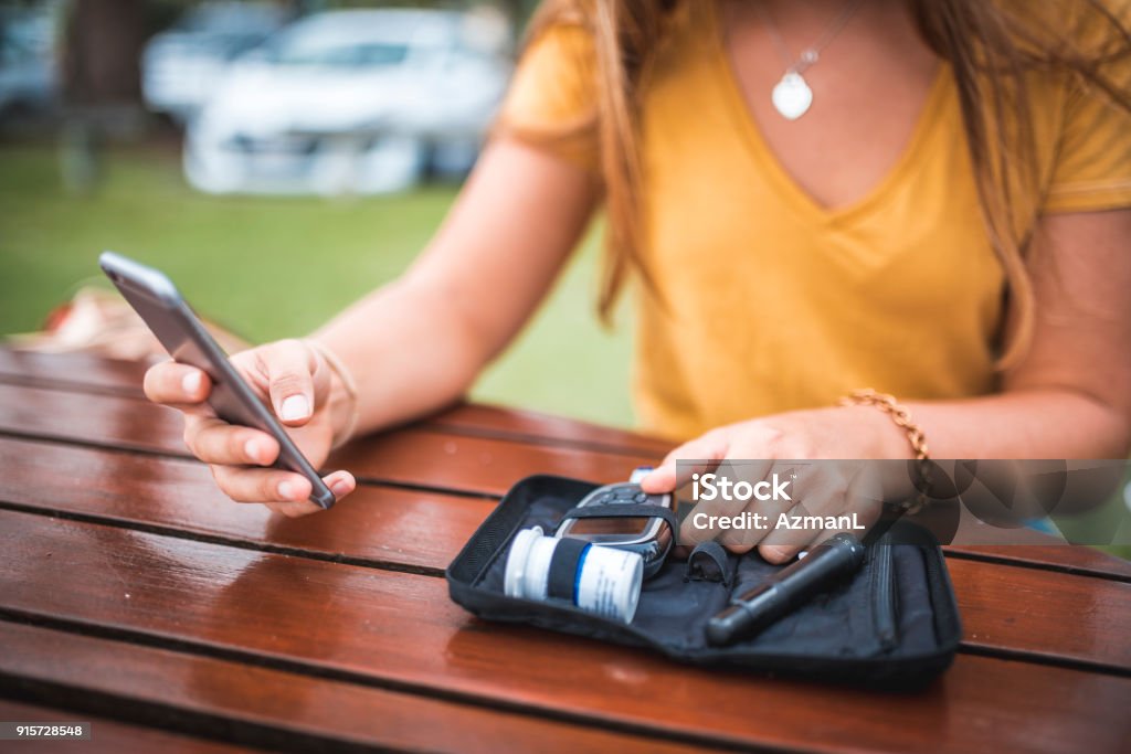 Jeune femme mesurant le niveau de sucre dans le sang et l’utilisation de téléphone portable - Photo de Diabète libre de droits