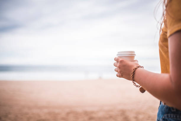 istock Young woman walking on the beach and holding coffee cup 915728570