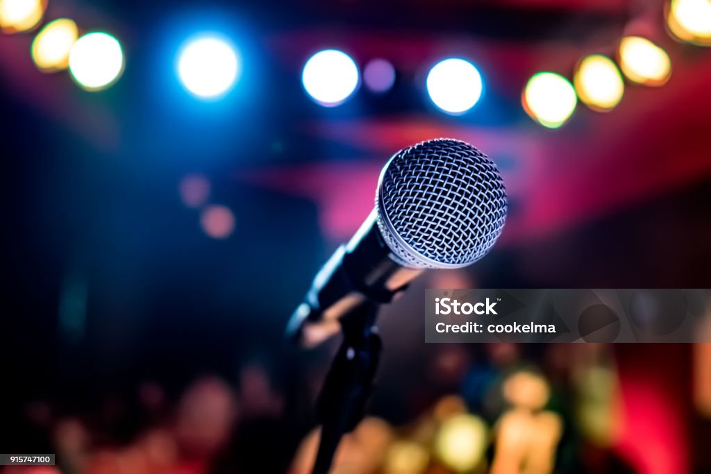 Microphone on stage against a background of auditorium. Public performance on stage Microphone on stage against a background of auditorium. Shallow depth of field. Public performance on stage. Microphone Stock Photo