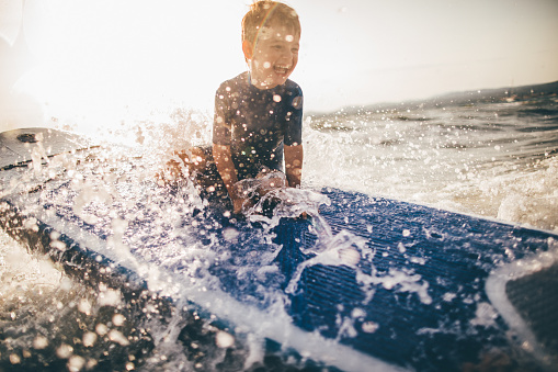 Photo of a cheerful little boy trying to stand up on a surfboard right before the wave strikes