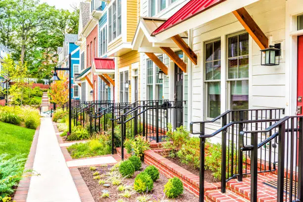 Photo of Row of colorful, red, yellow, blue, white, green painted residential townhouses, homes, houses with brick patio gardens in summer