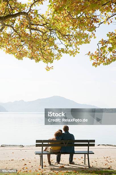 Vista Posteriore Del Giovane Coppia Seduta Abbracciato Su Panca Lakeside - Fotografie stock e altre immagini di Fidanzata