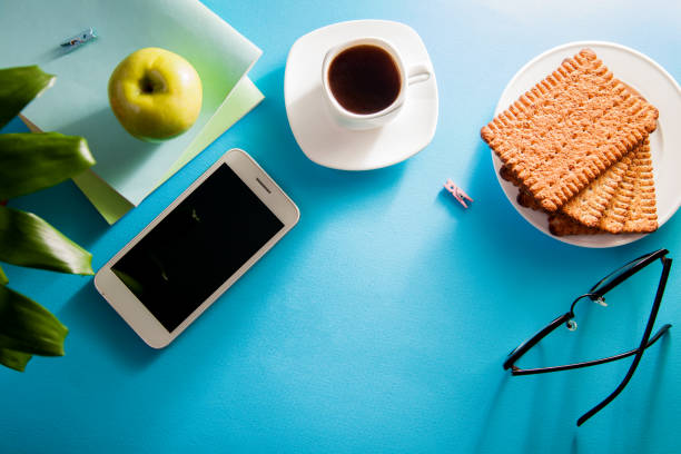 Workspace of a student on blue background. Studying with a cup of coffee and snacks, using a phone