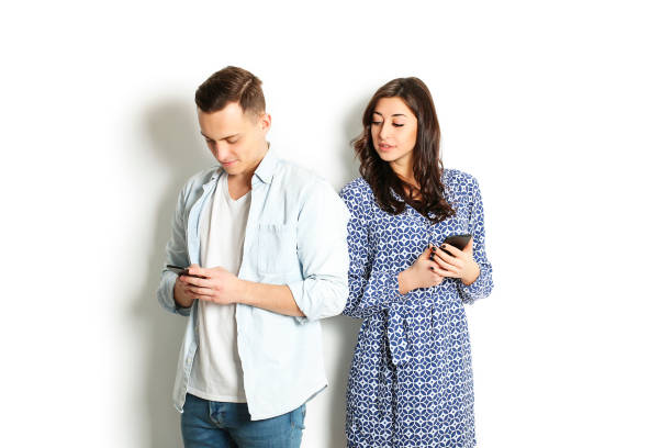 istock Jealous wife spying her husband mobile phone while he is reading a message. Technology & relationship concept. Modern romance troubles. Male and female online dating app. Swiping, browsing, surfing 915784834