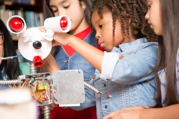 istock Elementary age school girls, teacher build robot in technology class. 915792514