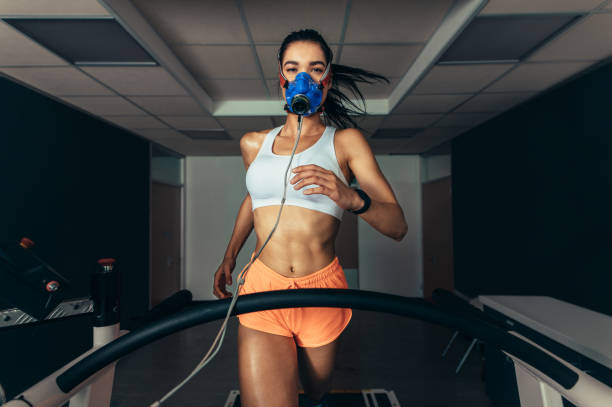Sportswoman with mask running on treadmill Sportswoman with mask running on treadmill. Female athlete in sports science lab measuring her performance and oxygen consumption. sports physical stock pictures, royalty-free photos & images
