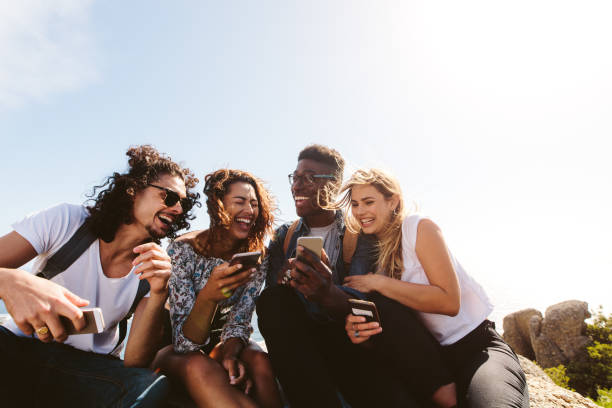 Group of people having fun on their holidays Young group of people sitting on top of mountain using smart phones and smiling. Diverse friends enjoying a day out. travel lifestyle stock pictures, royalty-free photos & images