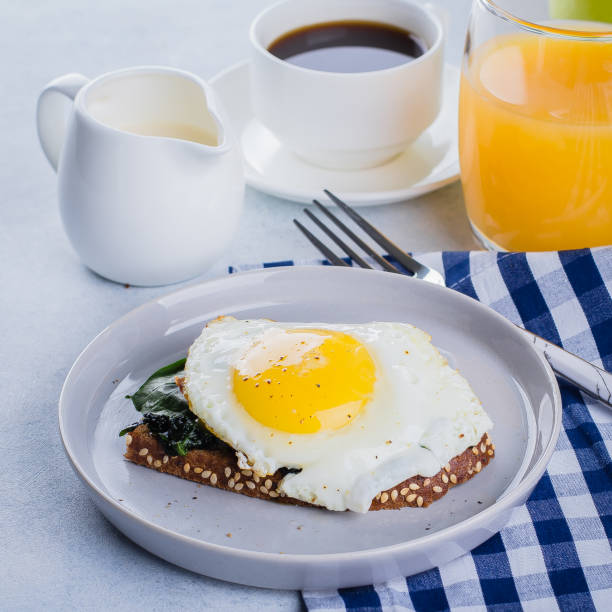 istock Rye bread toasts with fried spinach and egg with cup of coffee and orange juice on blue table background. Healthy Breakfast Food Concept. 915814222