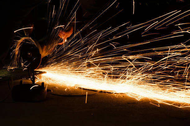 Worker cutting metal with grinder, sparks while grinding iron. Low key photography, space for text