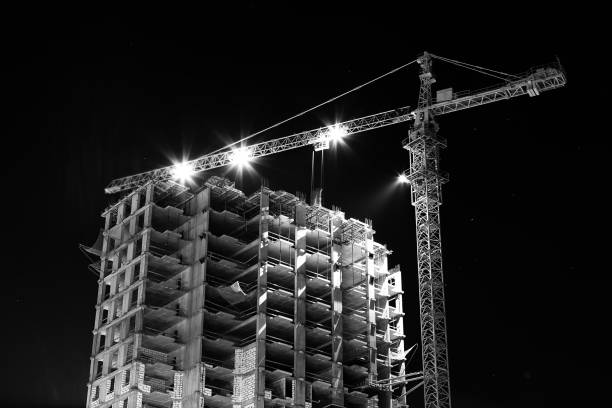 istock black and white Construction building site with tower cranes building under construction lighted with projectors at night from low angle 915831602
